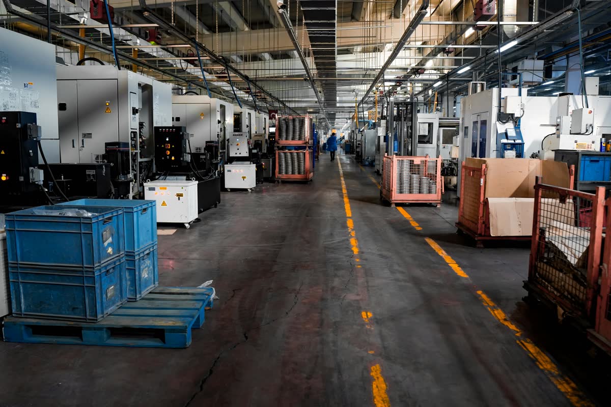 Manufacturing Equipment Obsolescence Planning  --  CNC precision machining shop floor with rows of enclosed machining centers, all requiring IT and OT asset documentation